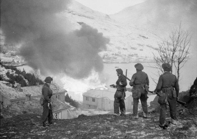 Foto: Britiske soldater ser et tysk ammunisjonslager i brann under Måløyraidet. Foto: Malindine, E G/Imperial War Museums. Offentlig eiendom.