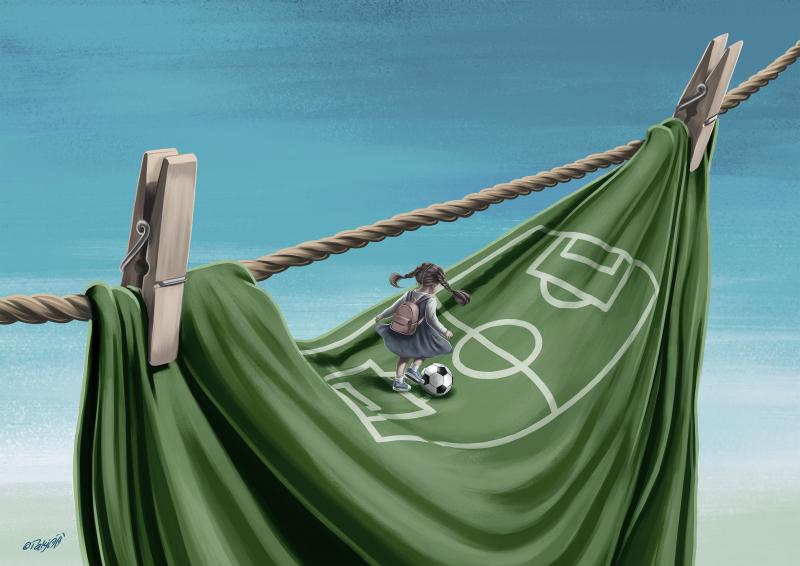 A girl carrying a backpack walks along a clothesline above a hanging cloth painted as a football field, with a football resting on it.