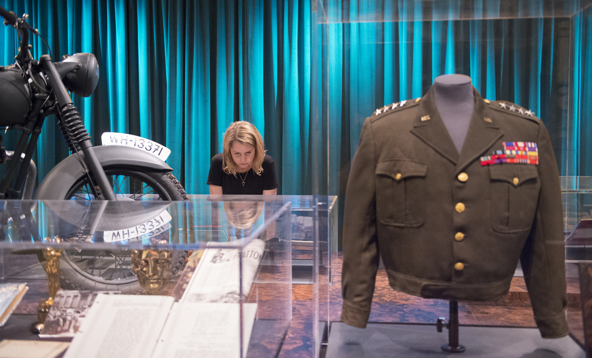 Exhibition View of "Real to Reel: A Century of War Movies". (LEFT) Replica motorbike from The Great Escape, Object: IWM (RIGHT) Patton costume worn by George C. Scott, Courtesy of Angels Costumes Photographed 28th June, 2016.