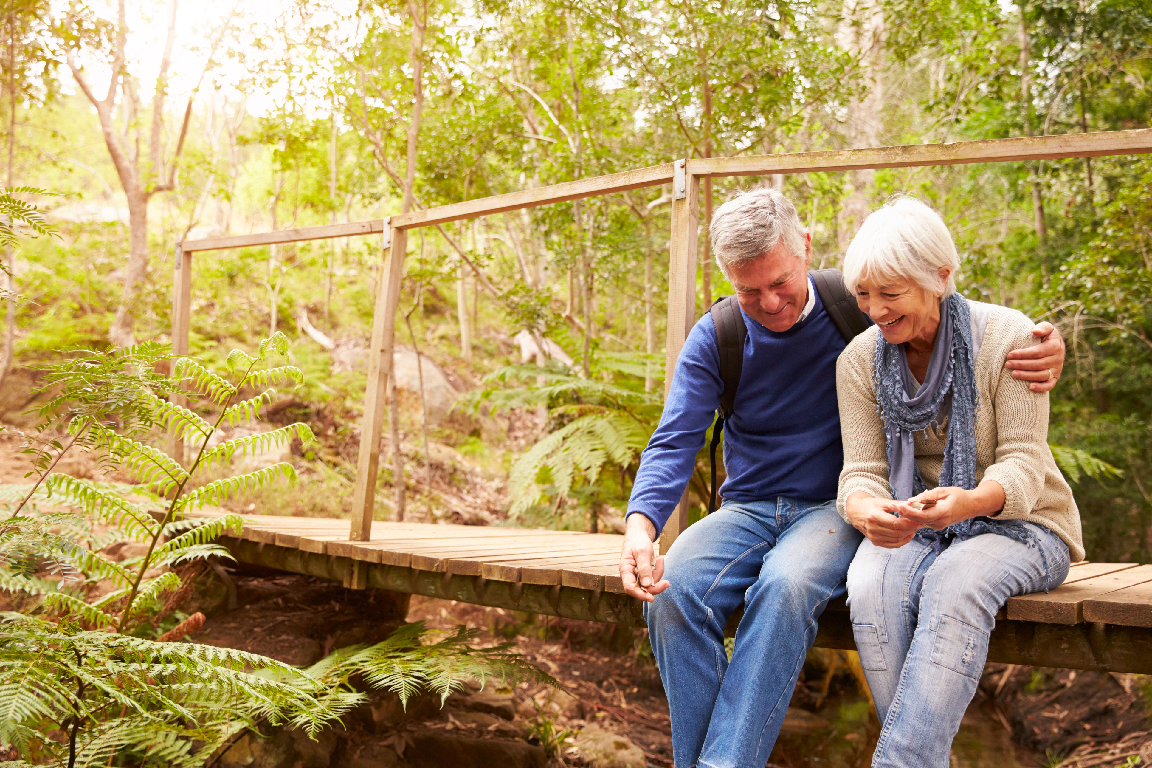 Happy senior couple sitting on bridge in forest, horizontal