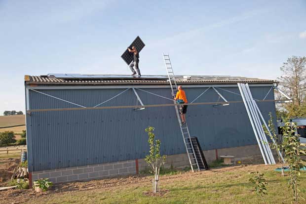 Two engineers installing photovoltaic solar PV panels on roof of steel barn Cotswolds UK