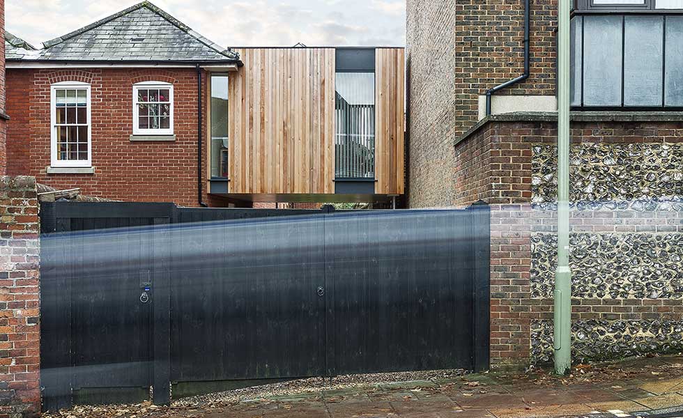 modern wooden panelled and glass extension behind black gate