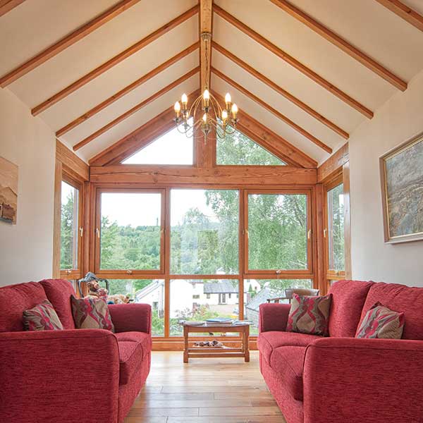 living room in self build with tiber beams and red settees and large wooden windows