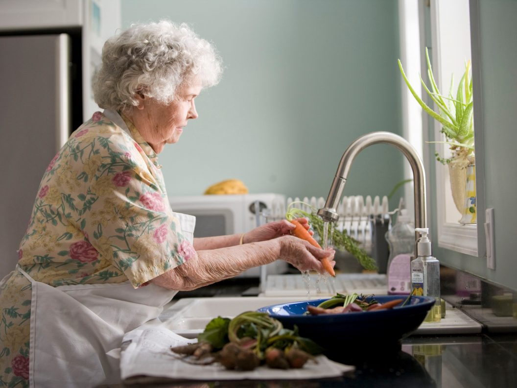 Oudere dame wast groenten in haar keuken