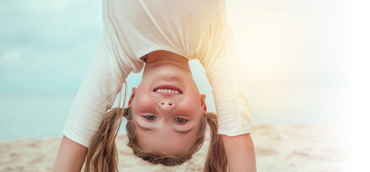 Kleines Mädchen lächelt beim Handstand am Strand.