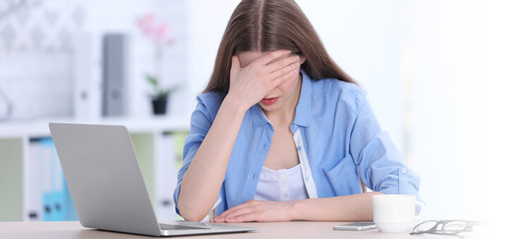 Junge Frau vor Laptop hält die Hand vor den Augen.