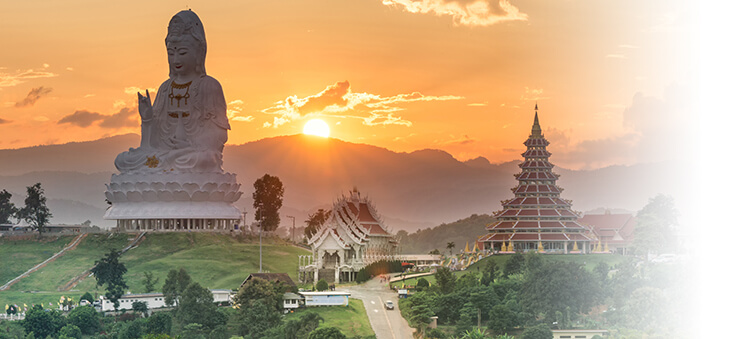 Riesige Buddhastatue und Tempel vor Hügellandschaft in Südostasien.