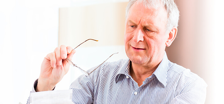 Älterer Mann hält Brille in der Hand.