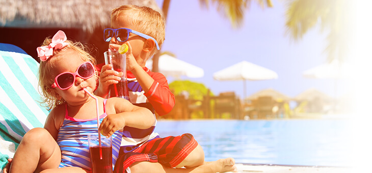 Zwei Kleinkinder sitzen mit Sonnenbrillen und Drinks am Pool.