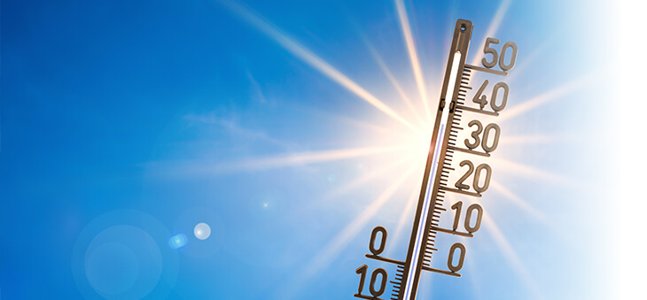 Thermometer vor blauem Himmel und Sonne.