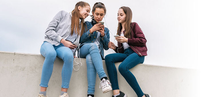 Drei jugendliche Mädchen mit Smartphones und Kopfhörern.