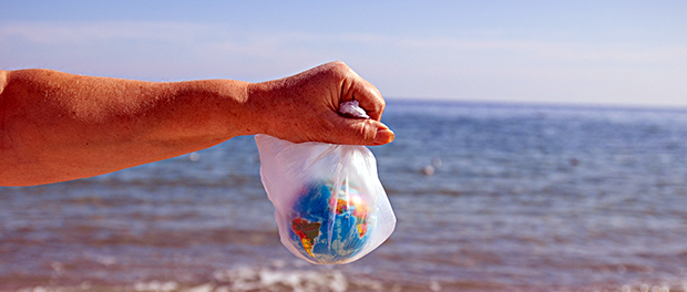 Woman hands a plastic bag and planet Earth on sea background.