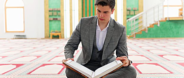 Religious muslim man praying inside the mosque and reading holy book koran.