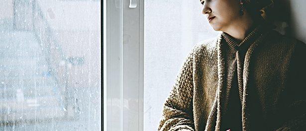Young Muslim woman sits on the window sill with flower bouquet in hands. Depressed middle-eastern female near the window at home. Lonely cheerless girl feeling stressed and waiting