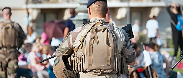 An unidentified Man in military uniform and with a military weapon patrolling the streets of the city during a public event.