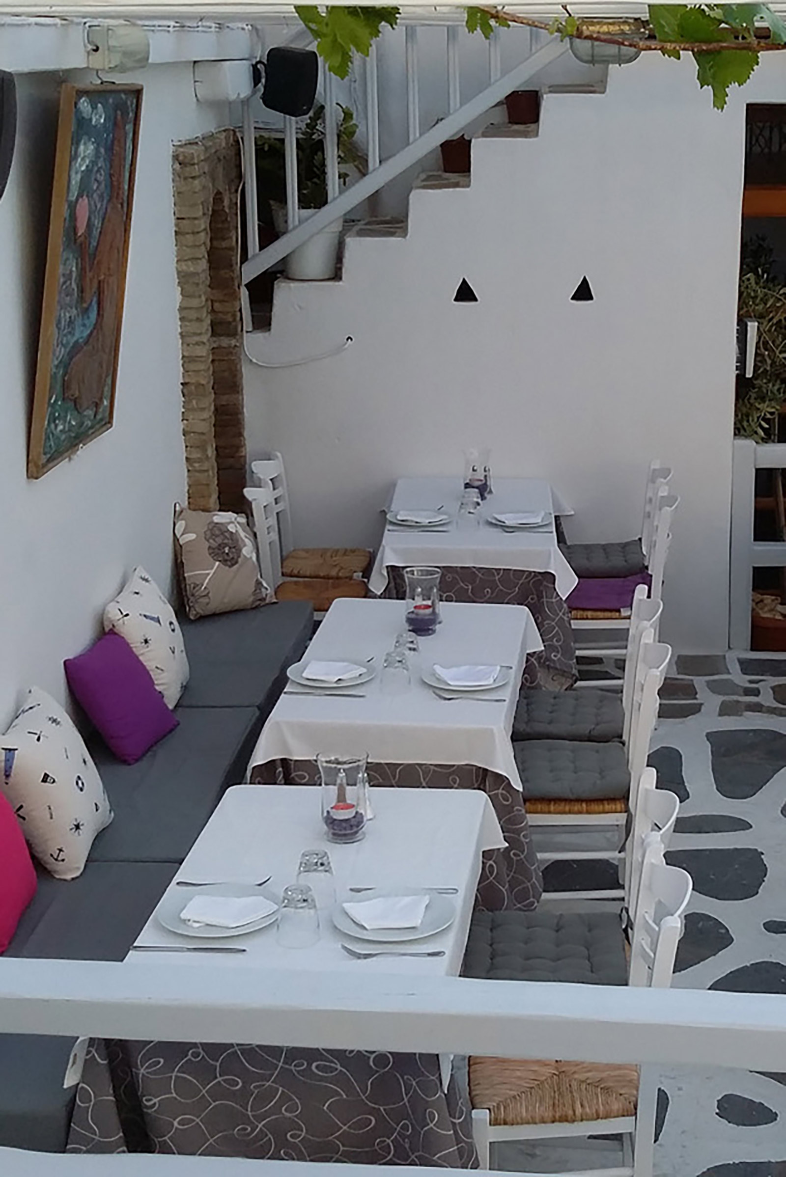 A “secret” garden full of flowers and roofed with vine leaves for total privacy, a large table on the street for a direct Mykonos Town feeling, an indoor air-conditioned large dining hall for ultra-hot summer nights and a beautiful veranda for candle-lit diners under the stars. - Image