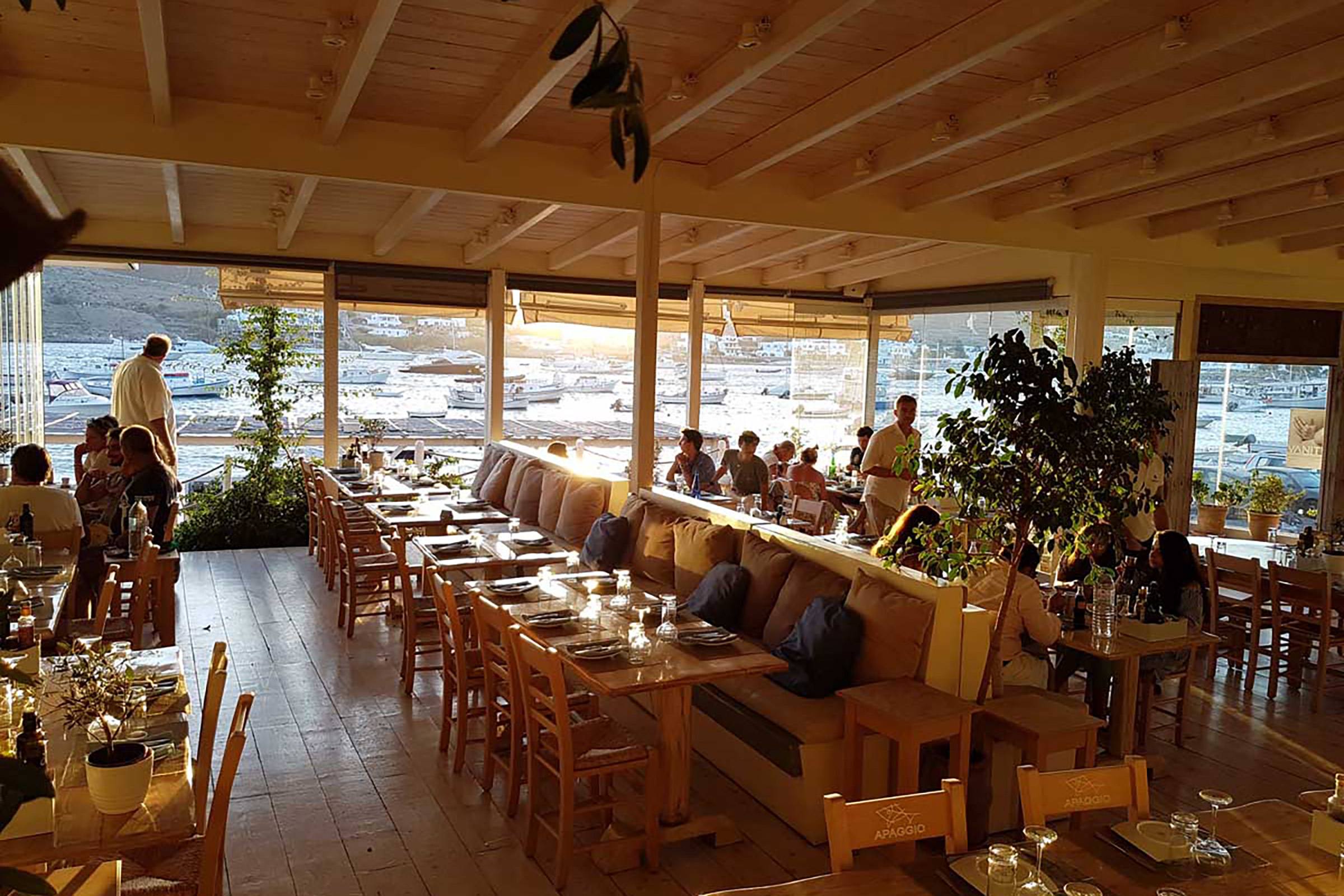 In a rather elegant setting and literally touching the sea, Apaggio restaurant, located on Ornos beach, has been serving Greece in a plate since 2013. It purposely keeps music at very low volume, so guests can dine listening to nothing but the magical sound of the sea. - Secondary Image