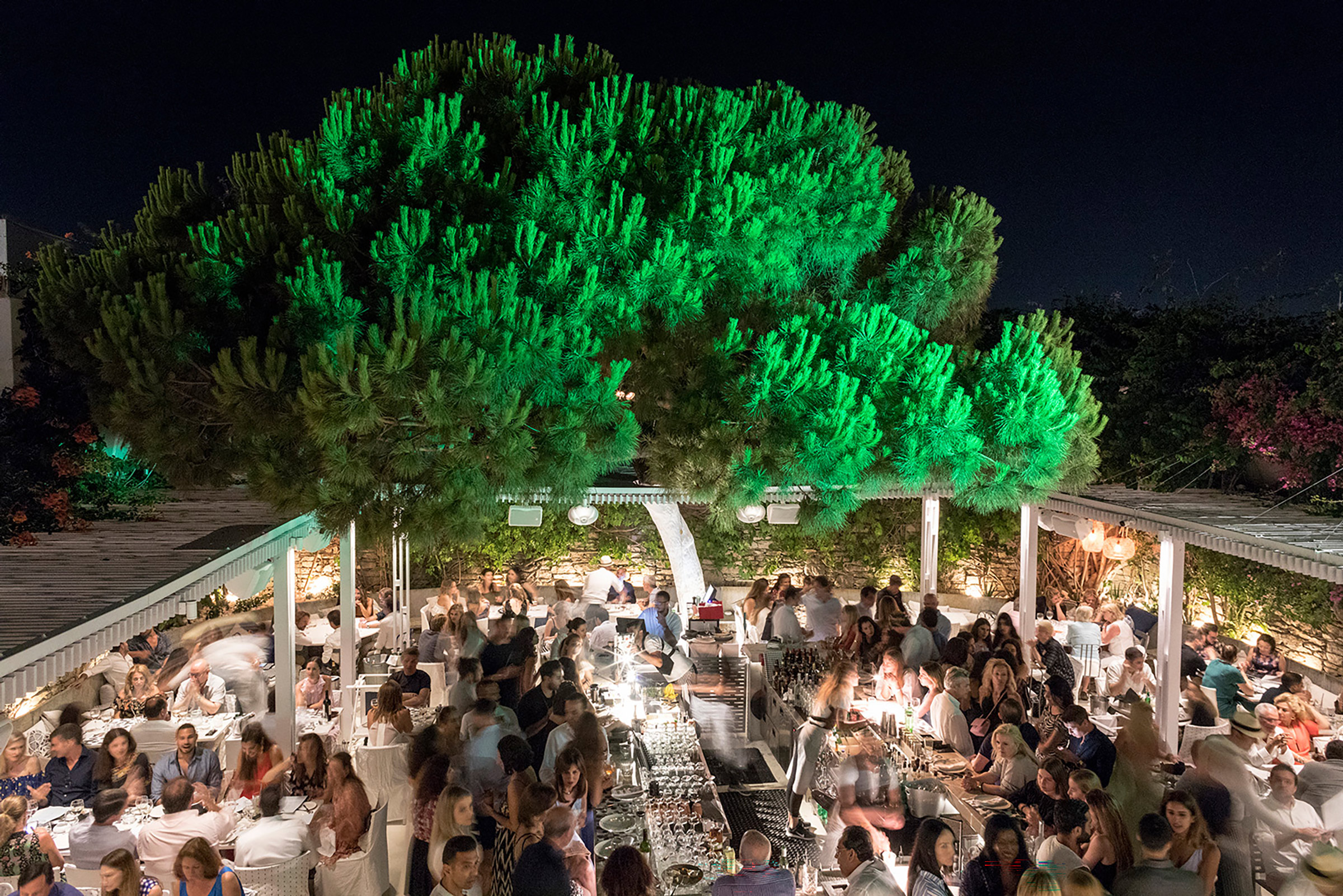 One of Mykonos’ most fashionable restaurant bars has been created by the world-famous designer and architect Paola Navone, combined with the personal touch of Greek high-design connoisseur, entrepreneur, and owner Nikos Varveris, which resulted in a stunning venue ticking all the right style boxes and speaking right to the heart of the elegant, sun-kissed, sophisticated crowd, frequenting this iconic meeting-point of the Mykonos’ nightlife. - Secondary Image