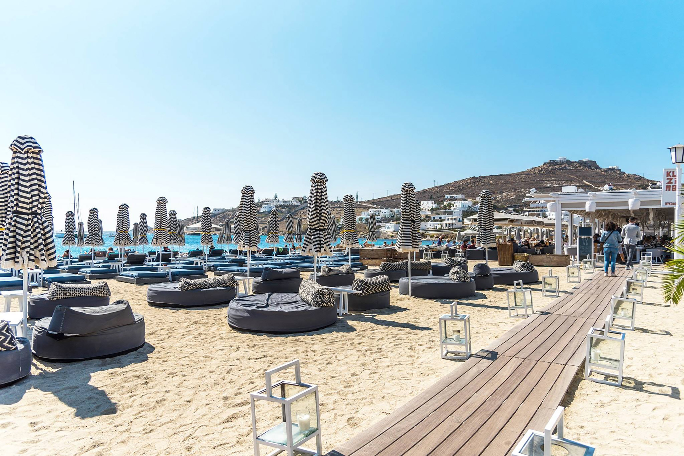 Nestled on the beautiful beach of Ornos, with its golden sand and turquoise waters, and displaying magnificent views of the sea and the bay, Kuzina is a cosmopolitan all-day beach restaurant offering Greek and Mediterranean dishes seen through a contemporary culinary eye. - Secondary Image