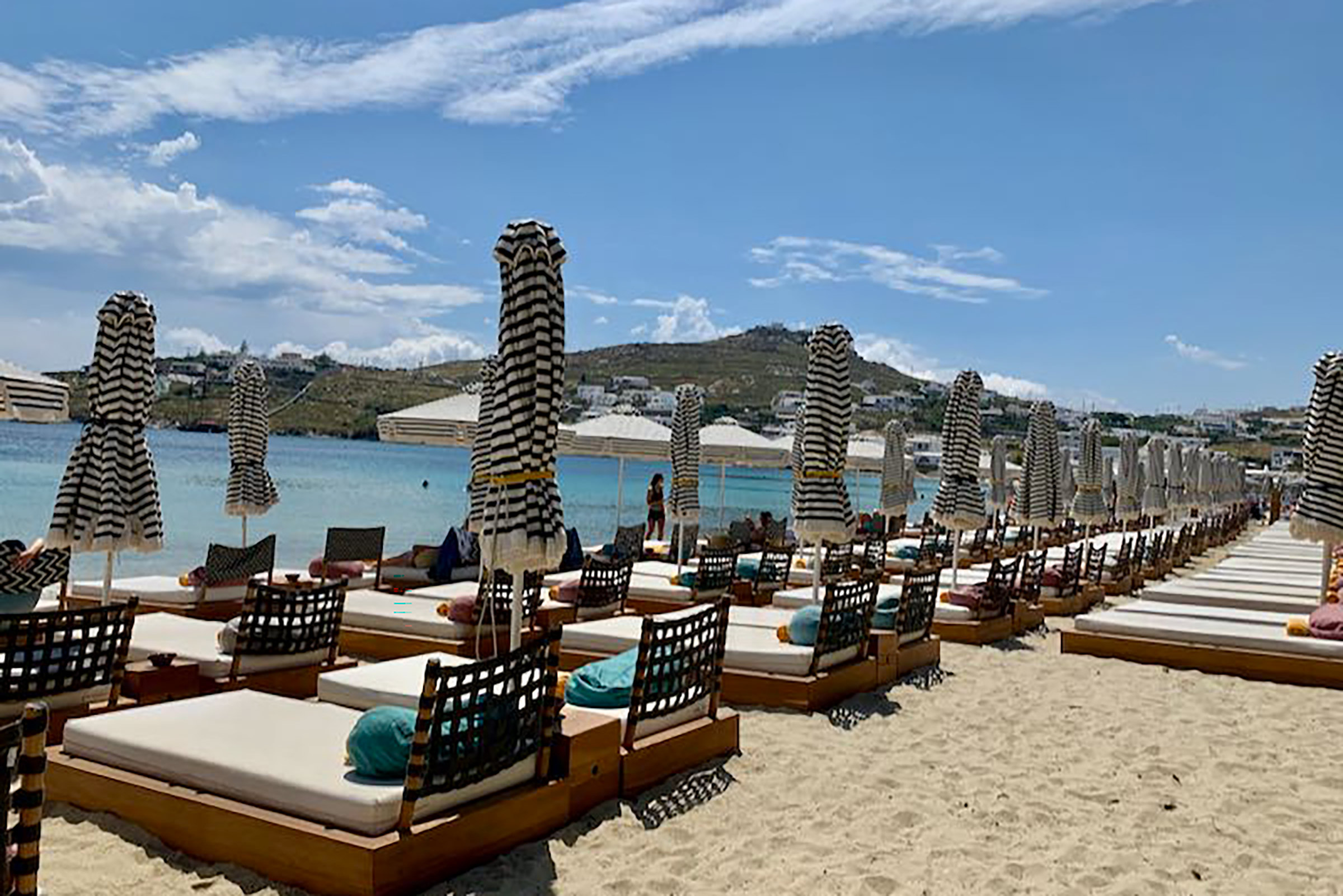 Constituting one of the best choices regarding all-day fun and dining on the island, Pasaji is located on the golden shore of Ornos (a hip, family-friendly, amazing beach) serving breakfast, brunch, lunch, dinner, drinks and cocktails from morning till night, under the mellow jams of the resident DJ. - Secondary Image