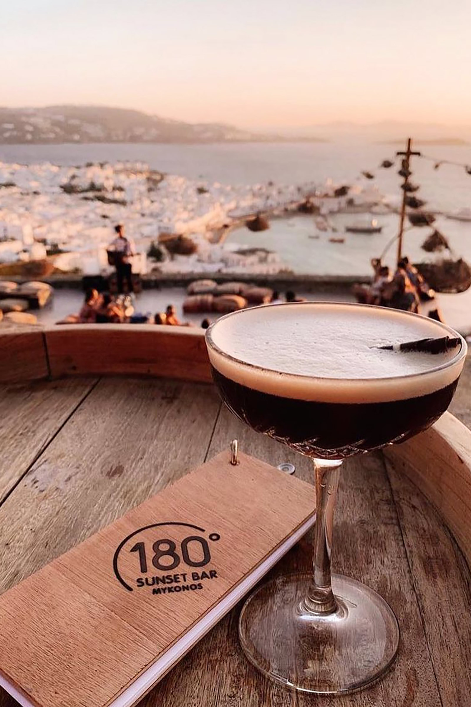 The extensive cocktail list boasts a wide collection of inspired signature recipes with wildflowers and fresh fruit lying in their core and adding the exotic touch anticipated in such a mesmerising setting, as well as the all-time classics expertly executed. The delicious dishes perfectly compliment the whole experience, as innovative tartars, crostinis, bao buns, burgers, premium meat cuts and many more delicacies give you something to nibble on as you enjoy the sun falling into the sea and the whitewashed houses of Mykonos Town painted in all shades of pink. - Image