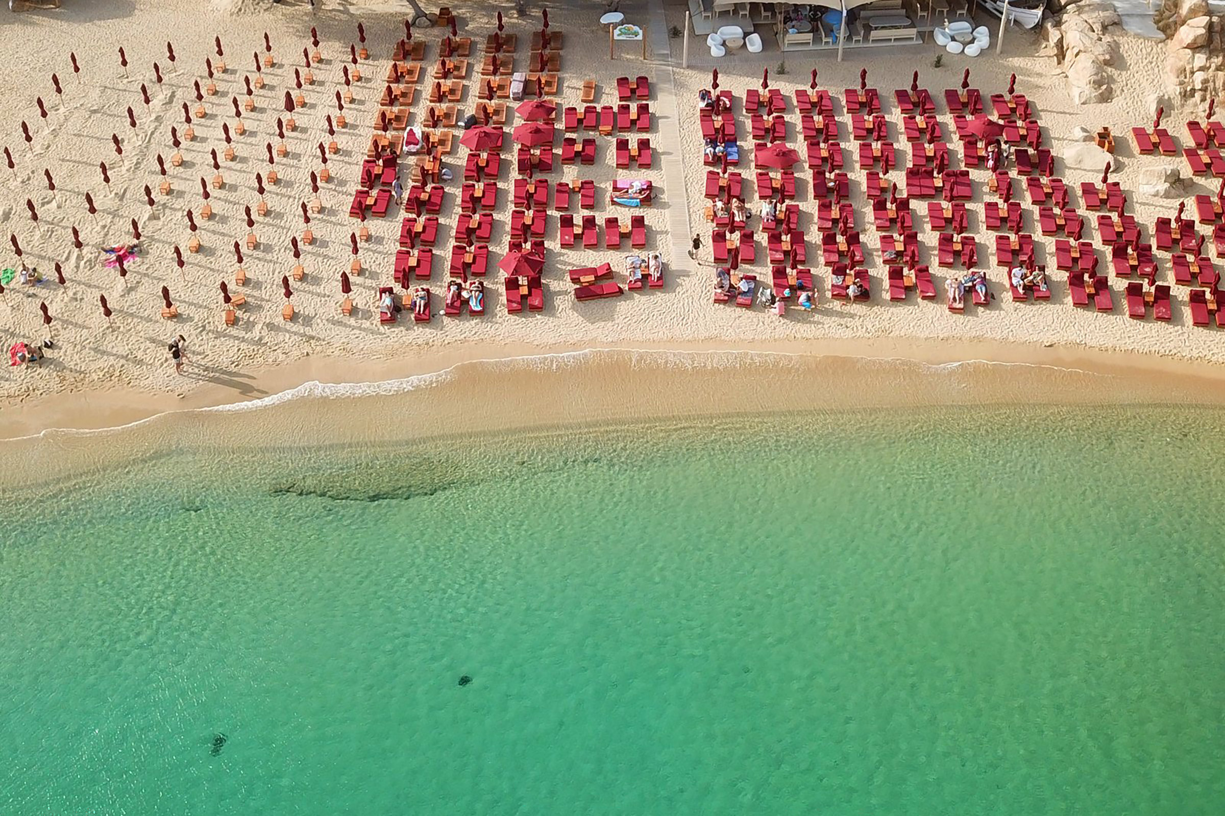 Early in the day the beach life is quite relaxed and cool, as everyone is taking their time to unwind and talk over last night’s big party in Mykonos Town, enjoy some water sports or just lay in the sand. - Secondary Image