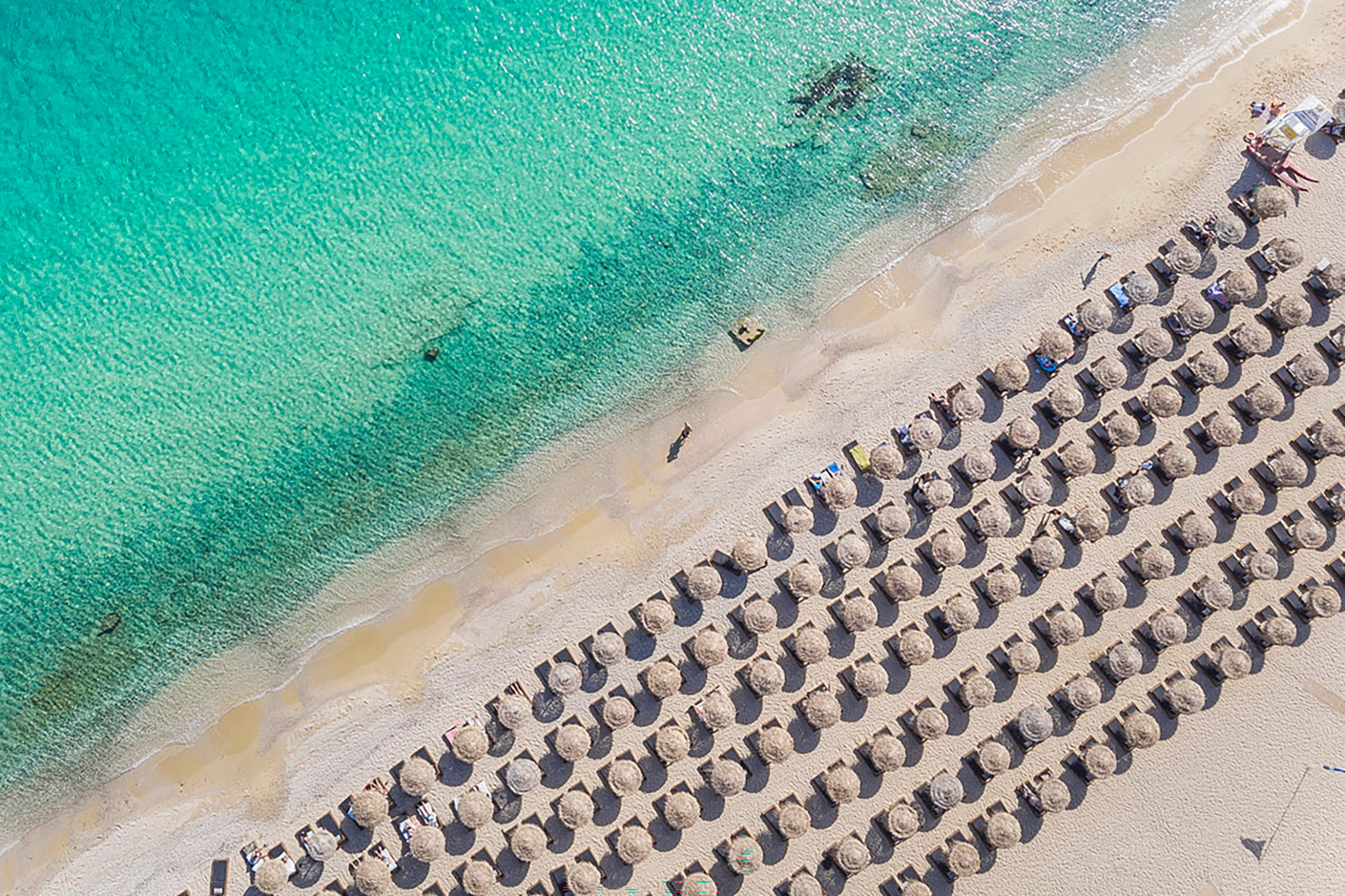 Relax all day on the golden sand of the pristine Elia beach, enjoy an innovative cocktail or a refreshing glass of wine, read your book, or just absorb the sun and the endless views, before heading for the robust wooden tables of the elegant restaurant awaiting to offer you a true feast for all the senses. - Secondary Image