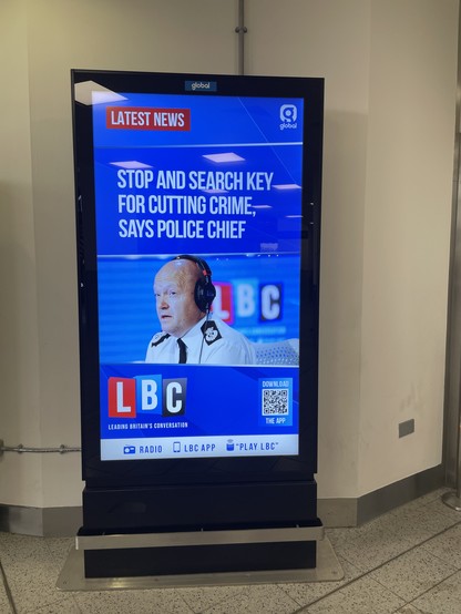 Video kiosk at Gatwick Airport with photo of cop and headline: Stop and search key for cutting crime says police chief – LBC