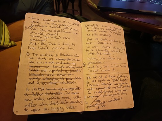 A notebook on a lab with parts of a speech written, scribbled out, etc. In the background is the backlit keyboard of a laptop.