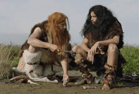 A caveman telling another to hammer a rock into the ground. Neither looks very intelligent.