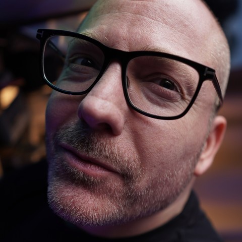 Extreme close-up of yours truly (generic white passing guy with shaved head, stubble, and black-rimmed glasses) looking slightly off camera with a smirk on his face. Is he deep in thought? Is he constipated? I guess we’ll never know.