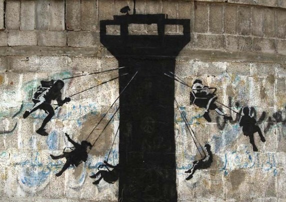 Graffiti on wall by Banksy: Children on a swing ride around a surveillance tower with a surveillance camera on it.