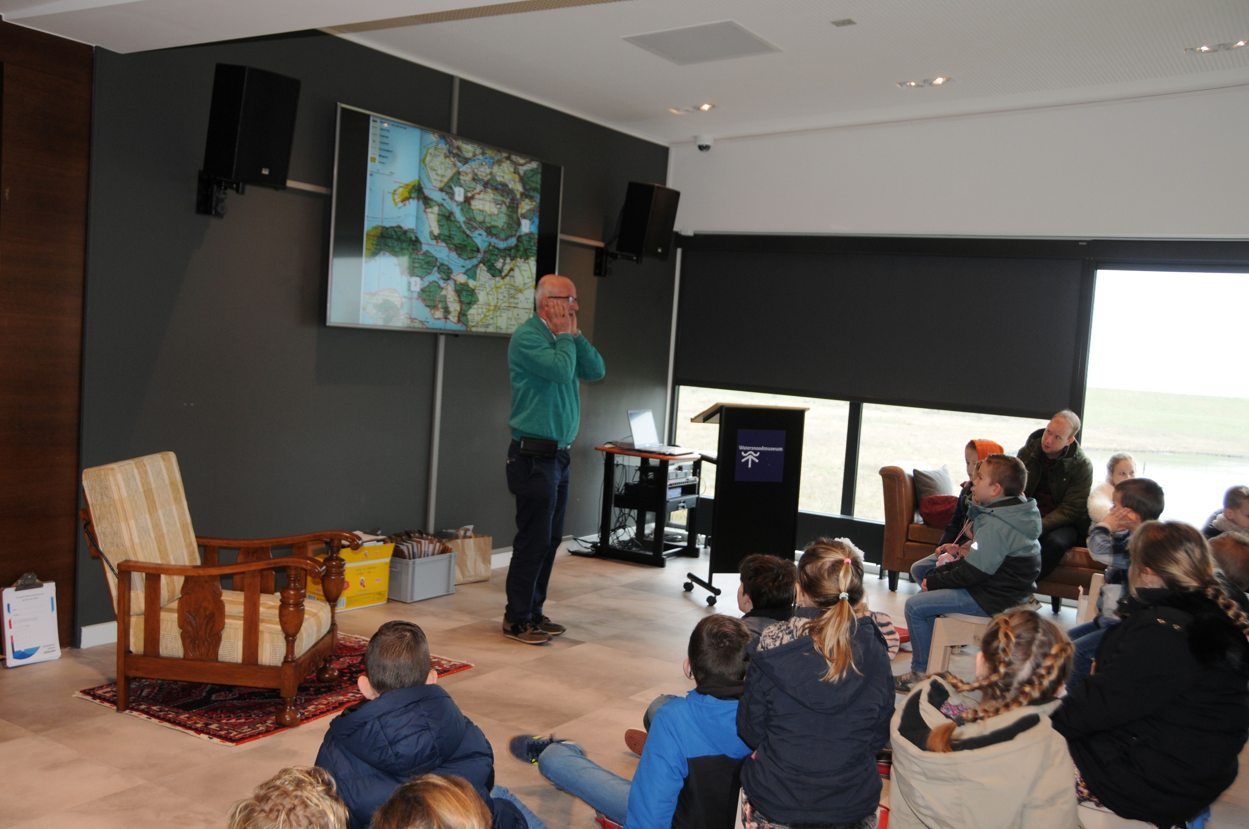 Kinderen luisteren en kijken naar een presentatie.
