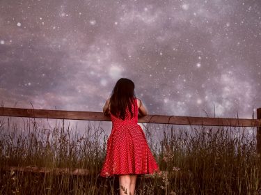 Mädchen lehnt an Zaun vor Sternenhimmel