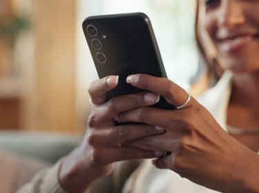 Junge Frau schaut lächelnd auf ihr Android-Handy.