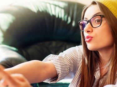 Frau mit gelber Mütze schießt mit dem Smartphone ein Selfie von sich.