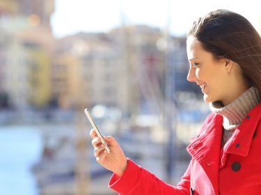 Frau im roten Mantel schaut auf ihr Smartphone