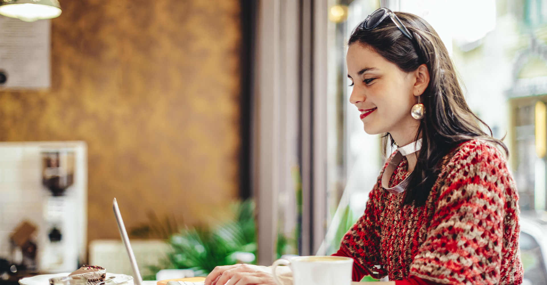 Junge Frau in roter Kleidung und Kaffee sitzt vor dem Laptop.