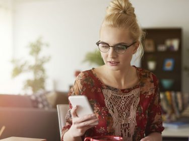 Frau mit blonden Haaren und Brille schaut ihr Smartphone.