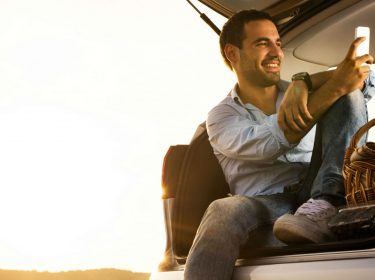 Mann sitzt im Kofferraum mit dem Smartphone.