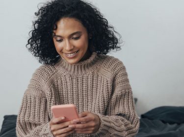 Frau schaut lächelnd auf ihr Handy.