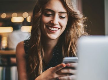 Was ist Galaxy Store? Junge Frau sitzt am Tisch und schaut auf ihr Smartphone.