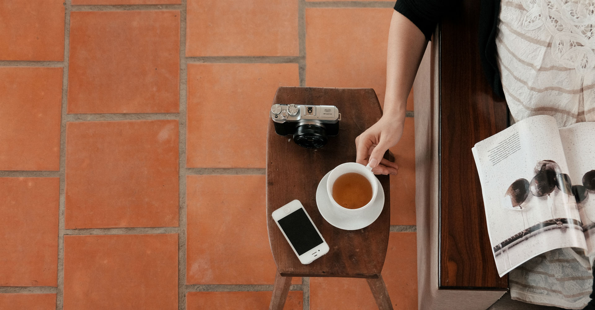 iPhone, Tasse Tee und Kamera liegen auf Hocker aus Holz.