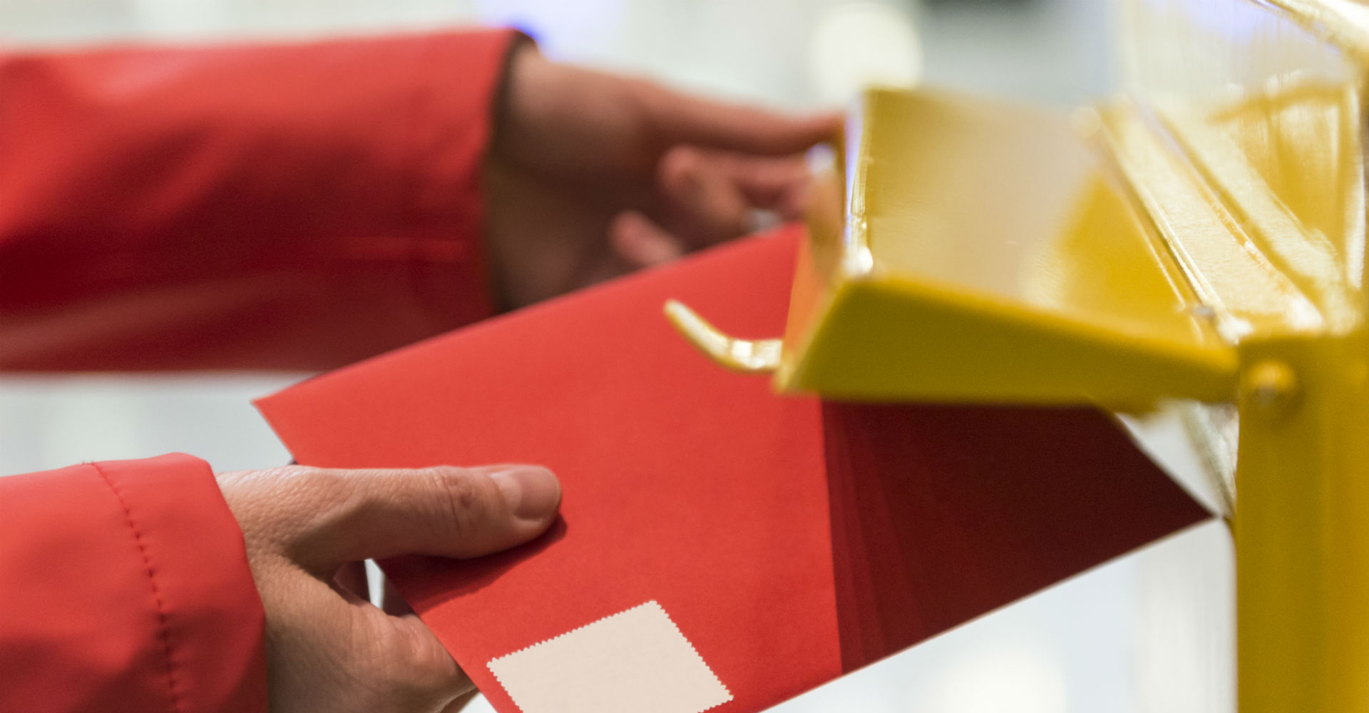 Roter Brief wird in gelben Briefkasten gesteckt.