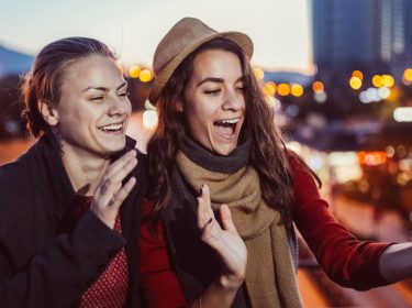 Zwei Freundinnen lächeln in die Smartphone-Kamera.