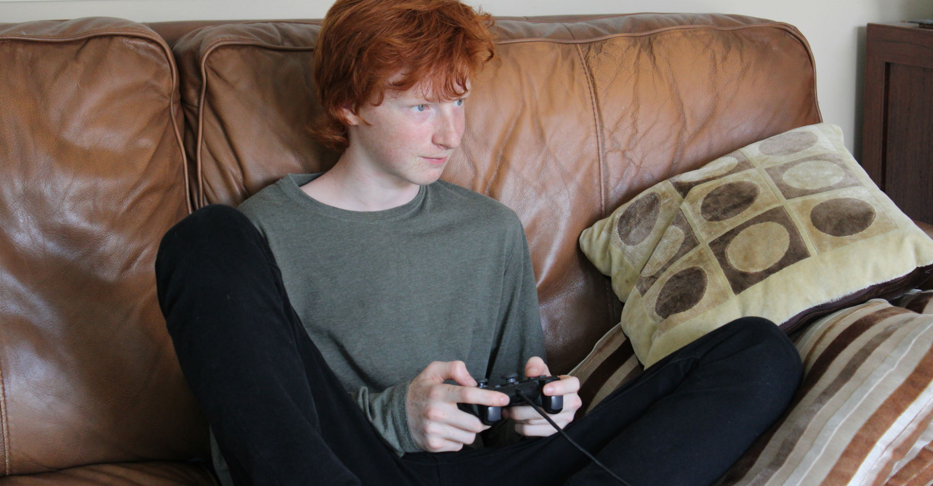 Junge mit roten Haaren zockt per Controller in der Hand.