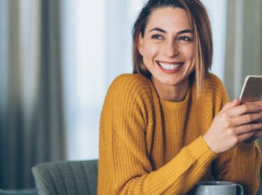 Frau lächelt und hält ein Smartphone in der Hand.