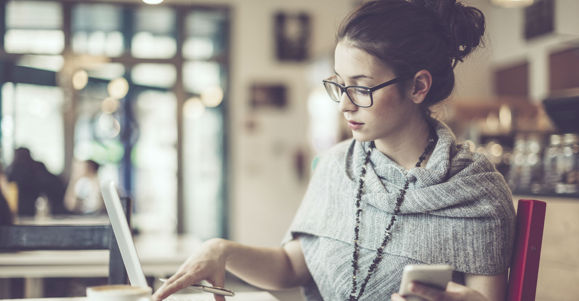 Frau arbeitet am Laptop und hält Smartphone in der Hand.