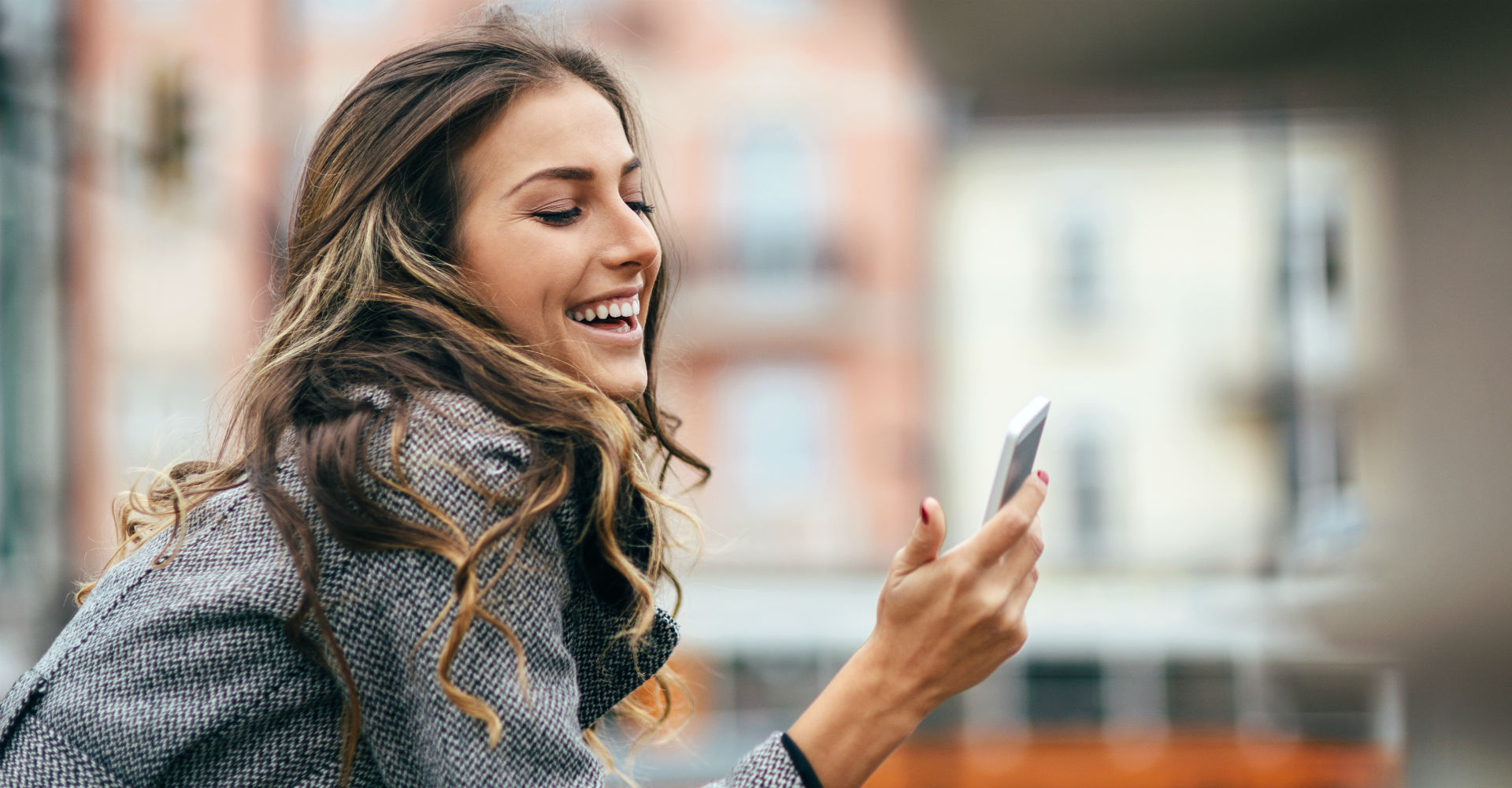 Junge Frau lächelt und schaut auf ihr Smartphone.