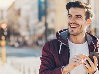 Junger Mann lächelt, während er ein Smartphone in der Hand hält.